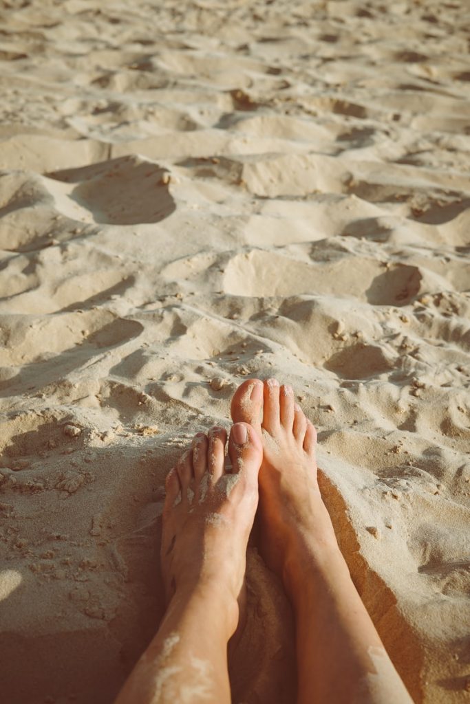 person's feet lying on sand